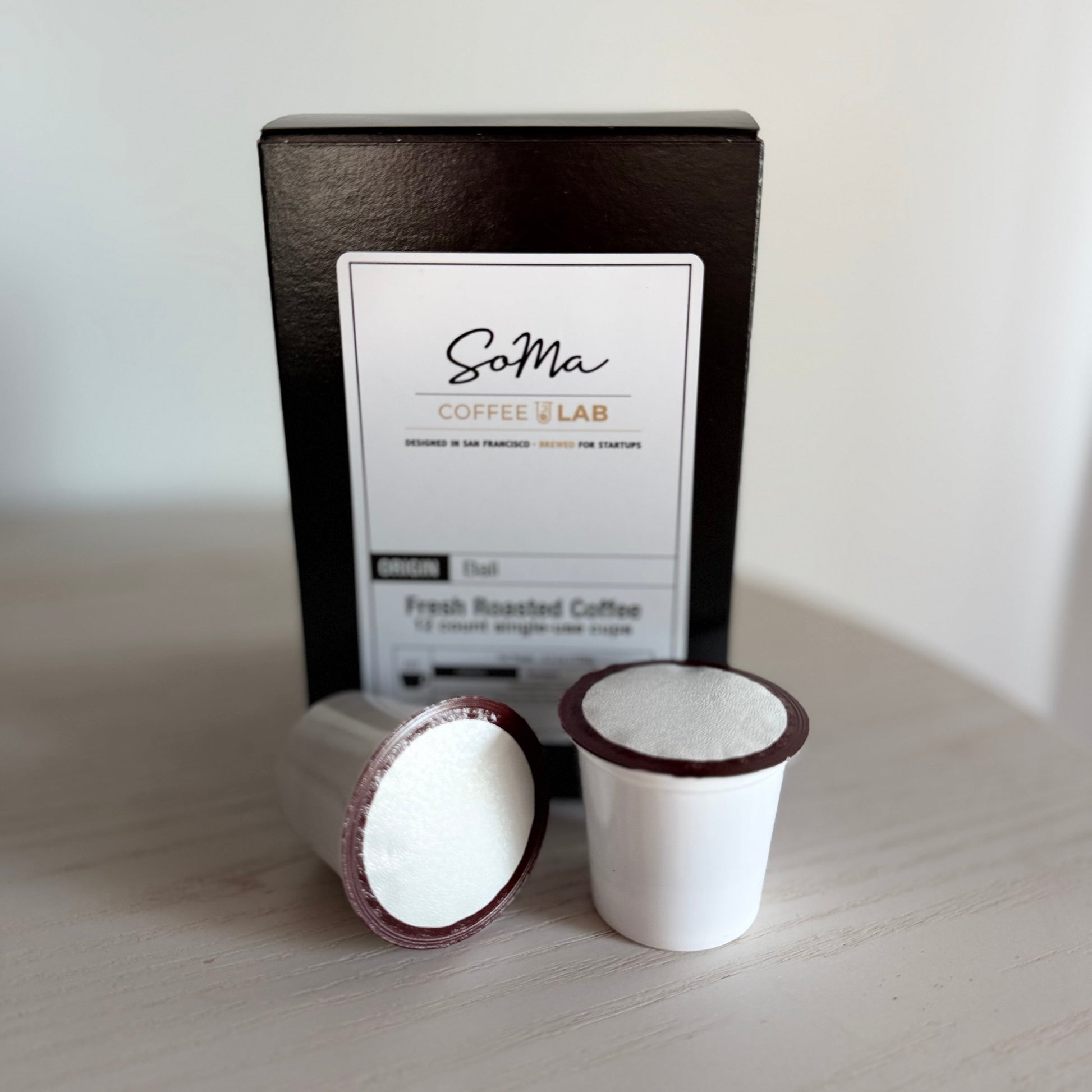 Two coffee pods and a black box labeled 'Soma Coffee Lab' on a light surface.